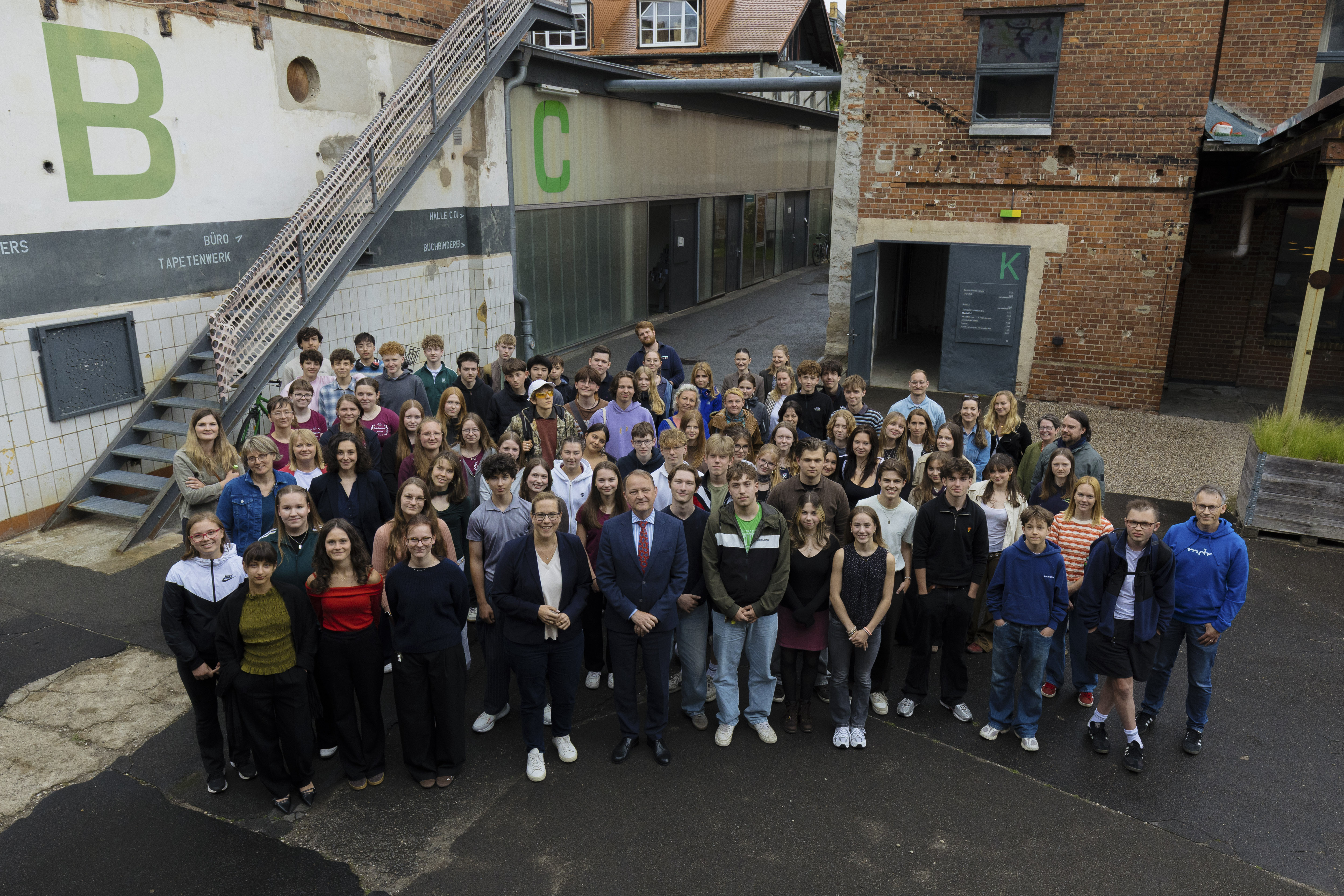KI generiert: Das Bild zeigt eine große Gruppe von Menschen, die vor einem Gebäude mit den Buchstaben "B" und "C" an der Wand posieren.