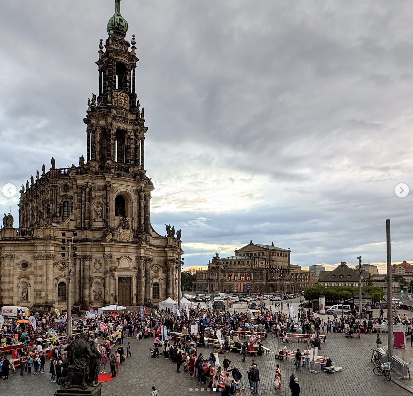 KI generiert: Das Bild zeigt eine große Menschenmenge auf einem Platz vor einer barocken Kirche bei bewölktem Himmel. Im Hintergrund ist ein weiteres historisches Gebäude zu sehen.