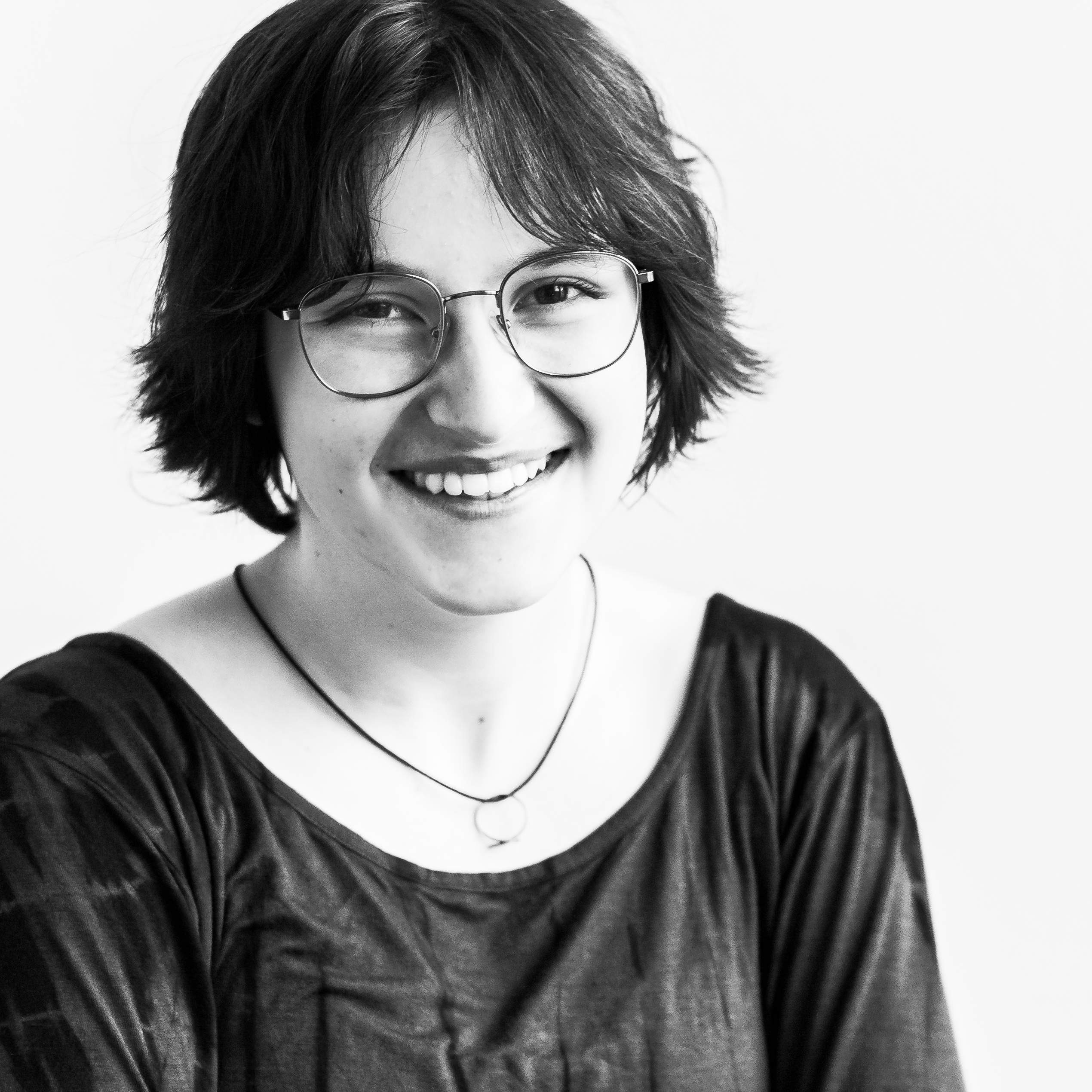 KI generiert: Das Bild zeigt eine lächelnde Person mit kurzen, dunklen Haaren und einer Brille, die ein gestreiftes Oberteil trägt.