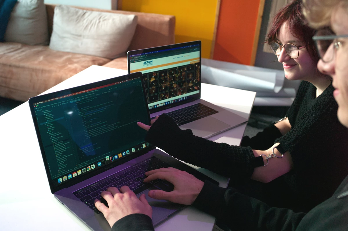 Zwei Personen sitzen lächelnd an Laptops und programmieren.