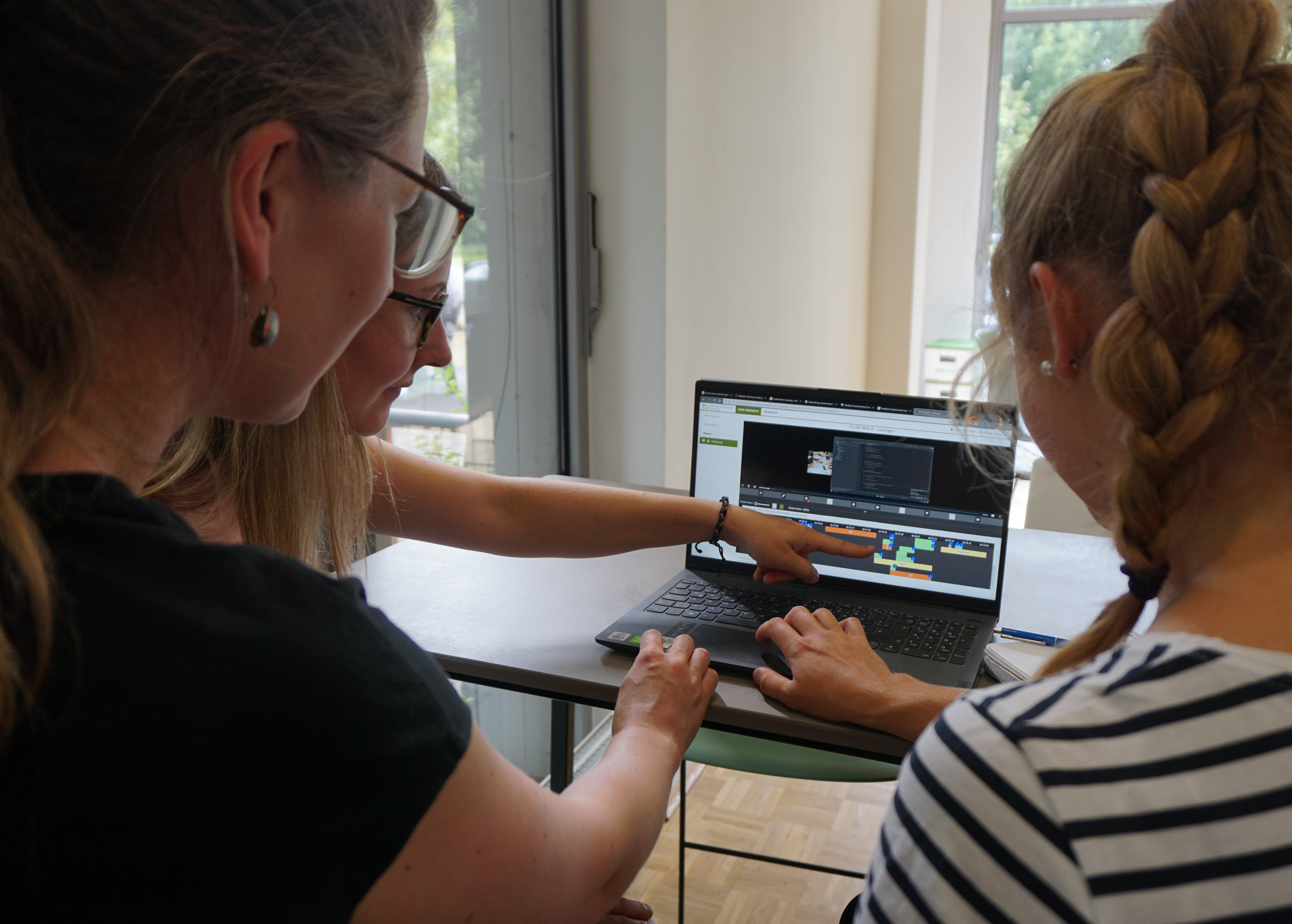 KI generiert: Das Bild zeigt drei Frauen, die gemeinsam an einem Laptop sitzen und etwas auf dem Bildschirm betrachten und besprechen. Eine der Frauen zeigt mit dem Finger auf den Bildschirm, während die anderen aufmerksam zuhören.