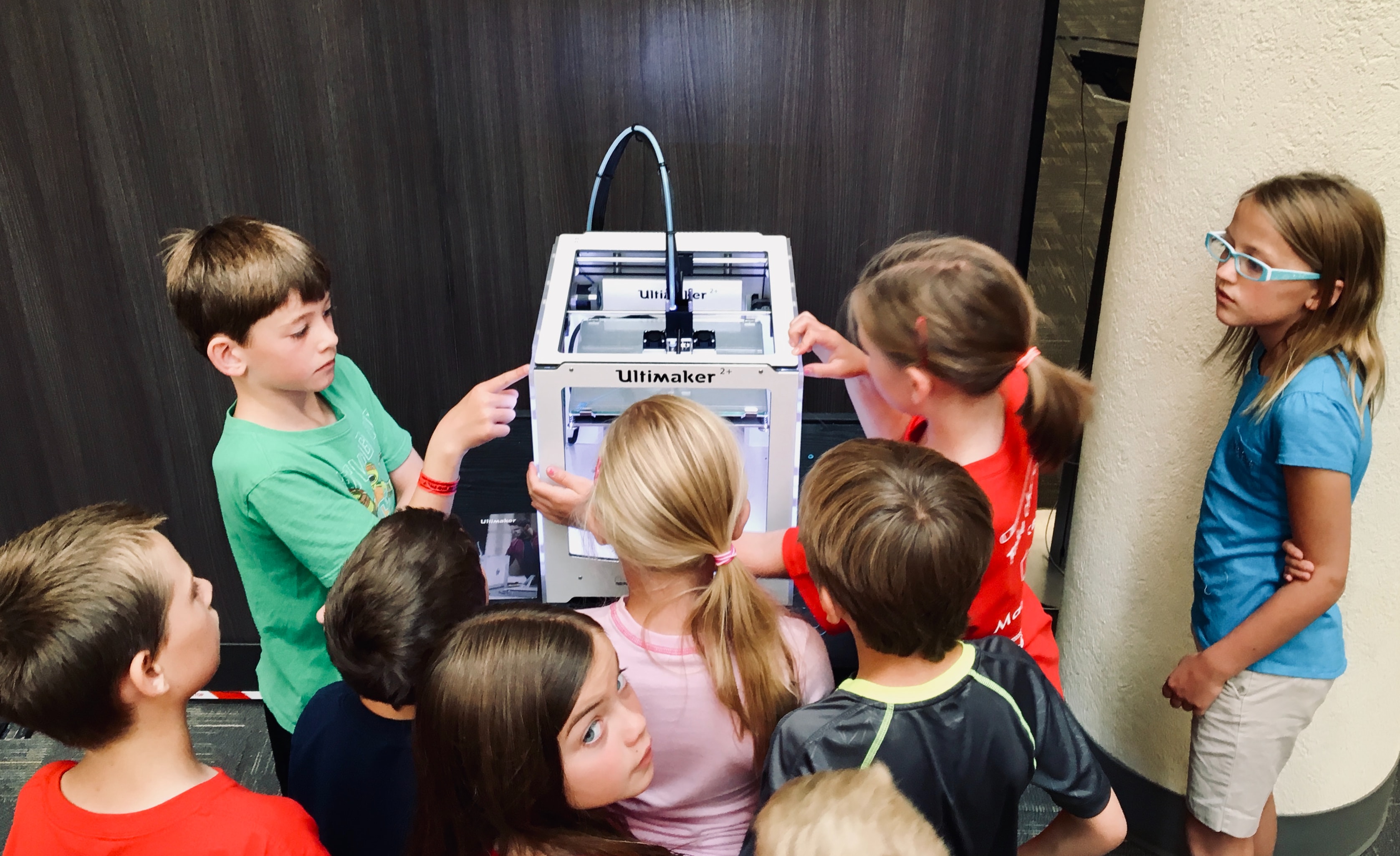 Foto einer Gruppe Kinder, die interessiert um einen 3D-Drucker stehen