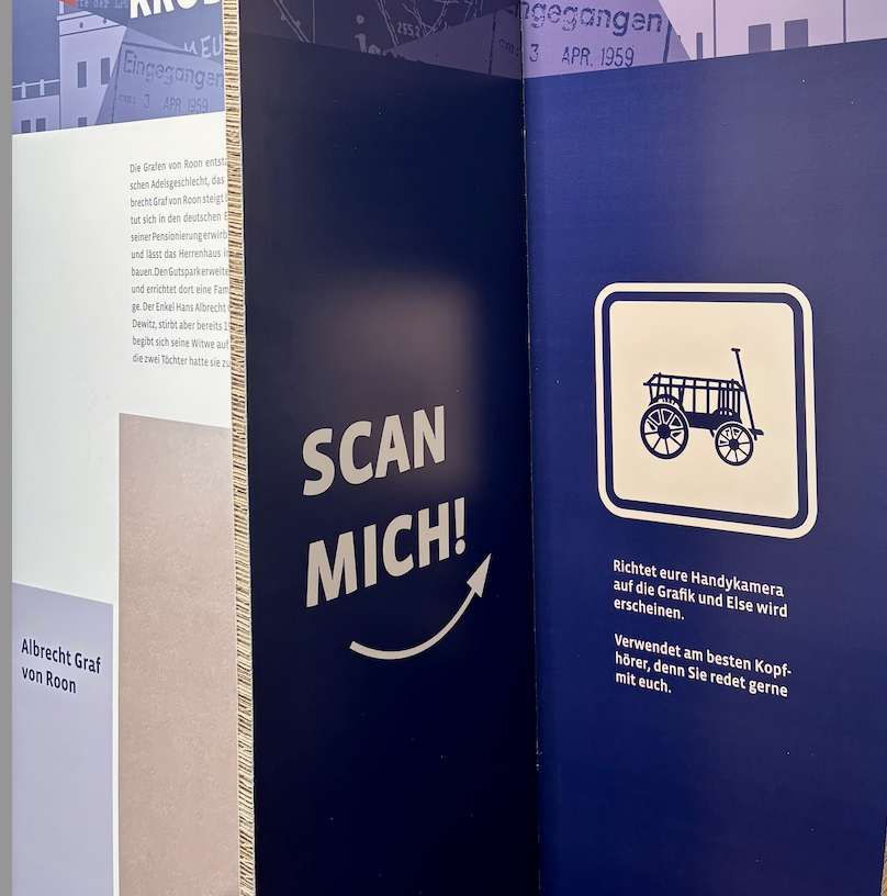 KI generiert: Das Bild zeigt eine Infotafel mit der Aufforderung "Scan mich!" und einer stilisierten Grafik eines Wagens, die gescannt werden kann, um weitere Informationen zu erhalten. Es gibt einen Hinweis, dass Kopfhörer verwendet werden sollen, da zusätzliche Erklärungen erfolgen.