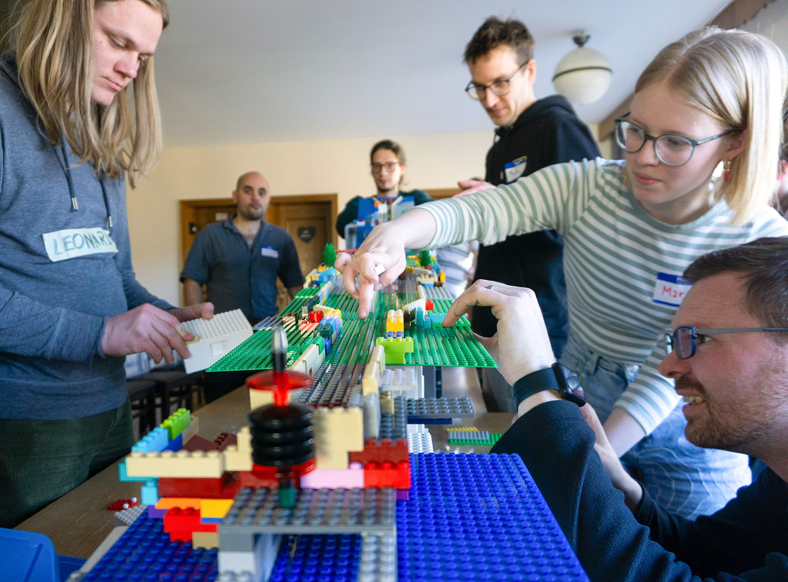 KI generiert: Eine Person steht vor einem Schreibtisch mit einem Computerbildschirm, der Code anzeigt. Im Hintergrund sind Poster mit den Zielen für nachhaltige Entwicklung zu sehen.