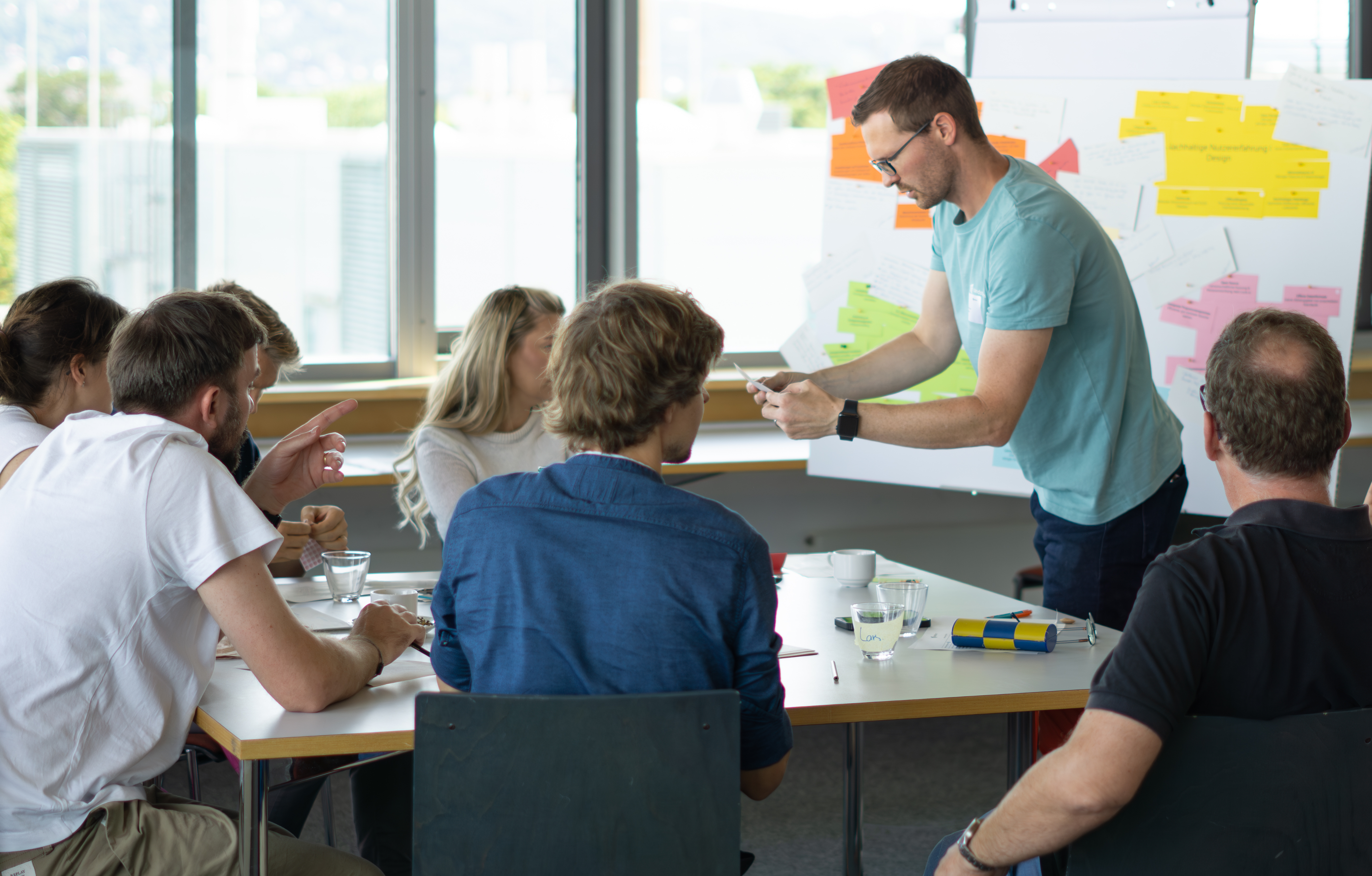 KI generiert: Das Bild zeigt eine Gruppe von Menschen in einer Besprechung oder Schulung, wobei eine Person vorne steht und etwas erklärt oder präsentiert.
