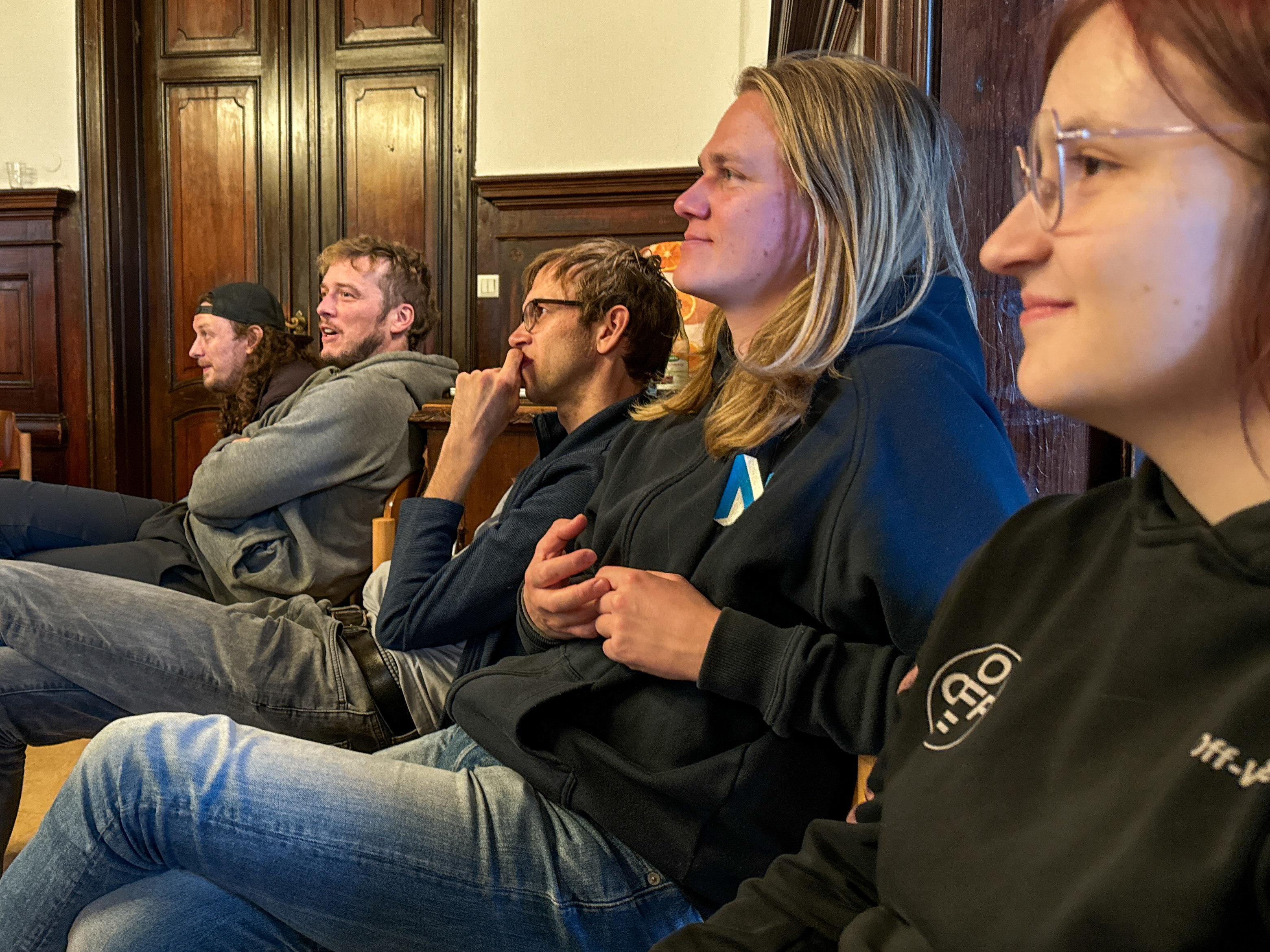 KI generiert: Eine Gruppe von Personen sitzt in einem Raum und richtet ihre Aufmerksamkeit in eine gemeinsame Richtung, vermutlich zu einer Präsentation oder Diskussion. Im Vordergrund befinden sich fünf Personen, die entspannt und konzentriert wirken.