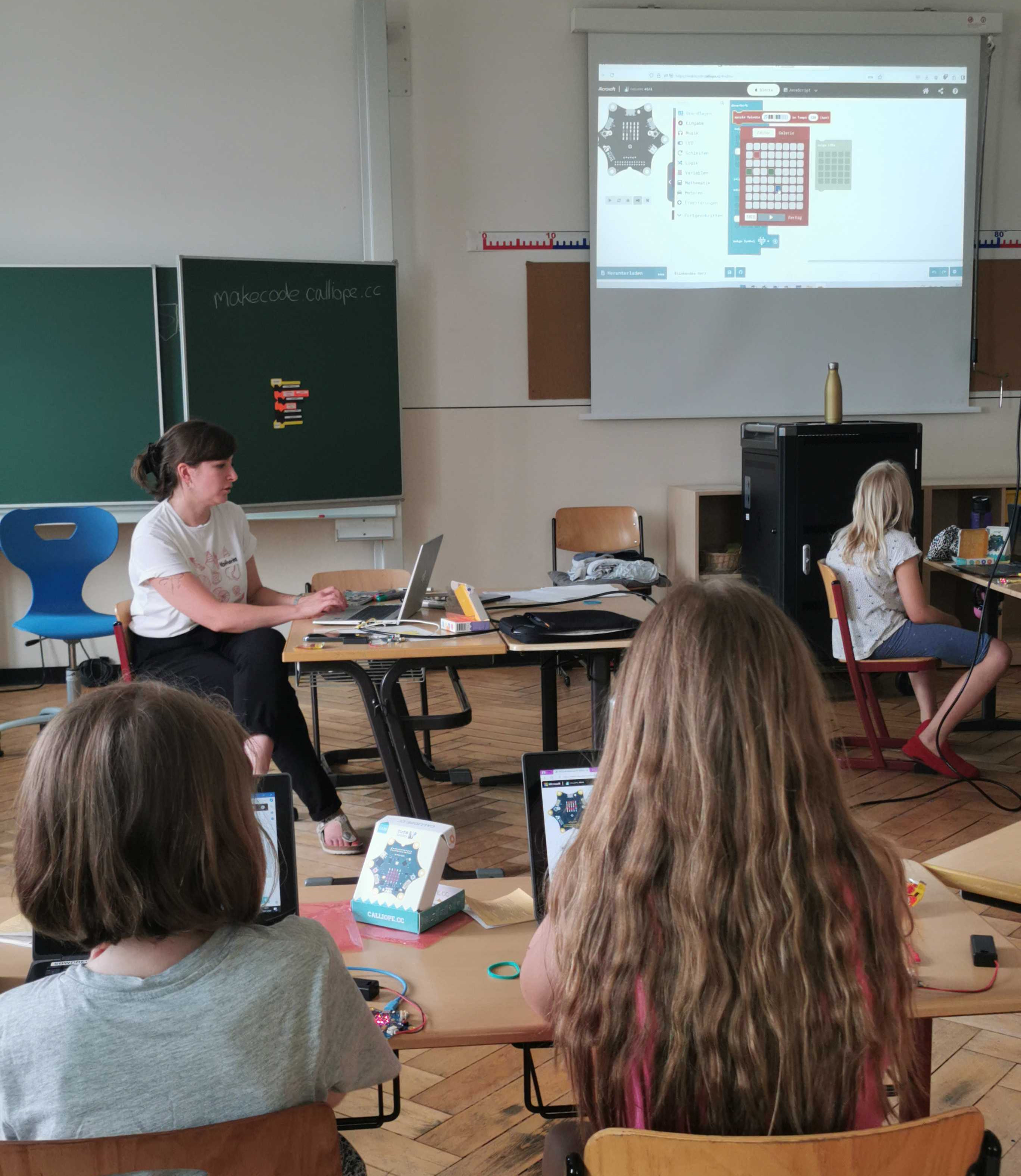 Im Klassenraum schauen Schülerinnen mit dem Rücken zur Kamera zu Katharina