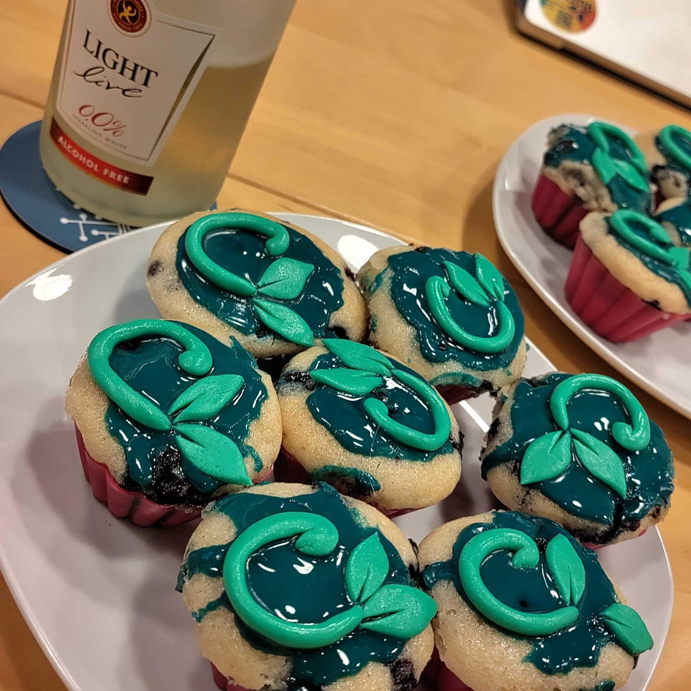 KI generiert: Das Bild zeigt dekorierte Cupcakes mit grüner Verzierung und einer Flasche alkoholfreien Getränks im Hintergrund.