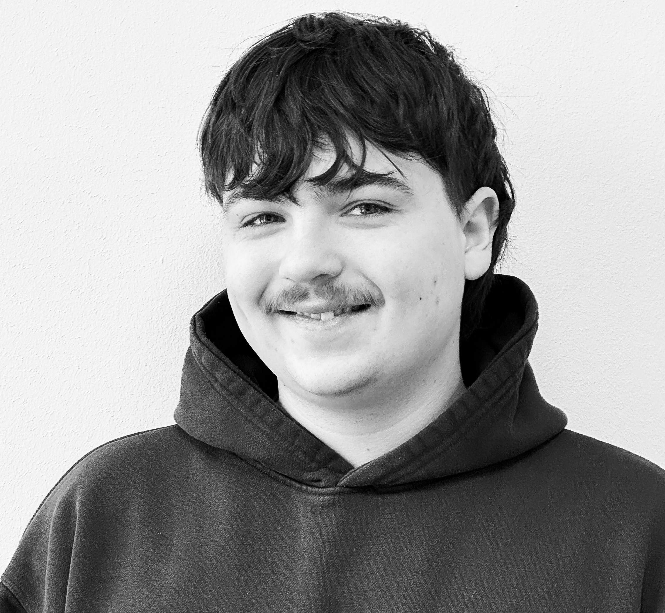 KI generiert: Ein schwarz-weißes Porträt eines lächelnden jungen Mannes in einem Kapuzenpullover vor einem neutralen Hintergrund.