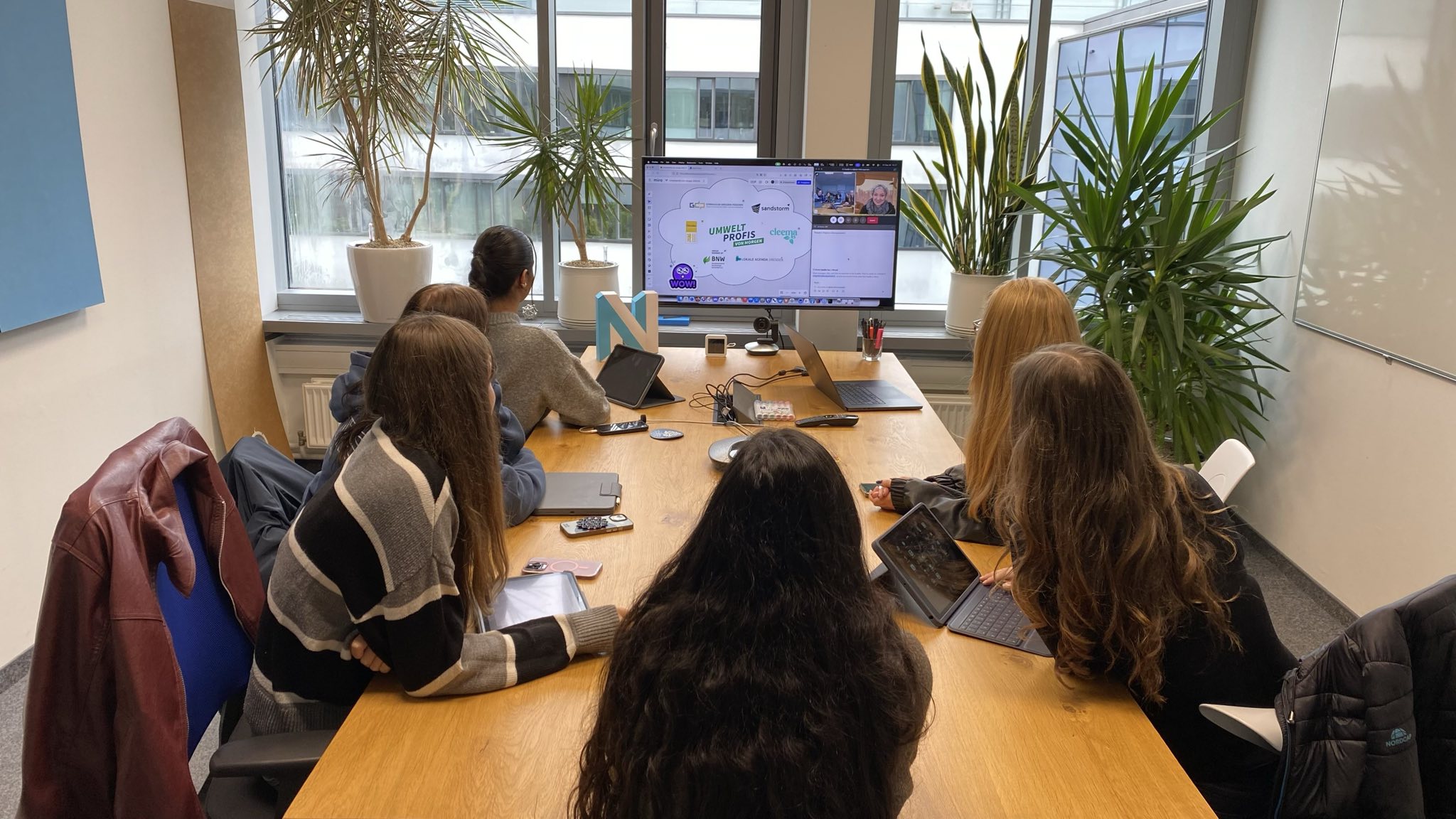 KI generiert: Eine Gruppe von Menschen sitzt in einem Konferenzraum und schaut auf einen Bildschirm, der eine Präsentation anzeigt.
