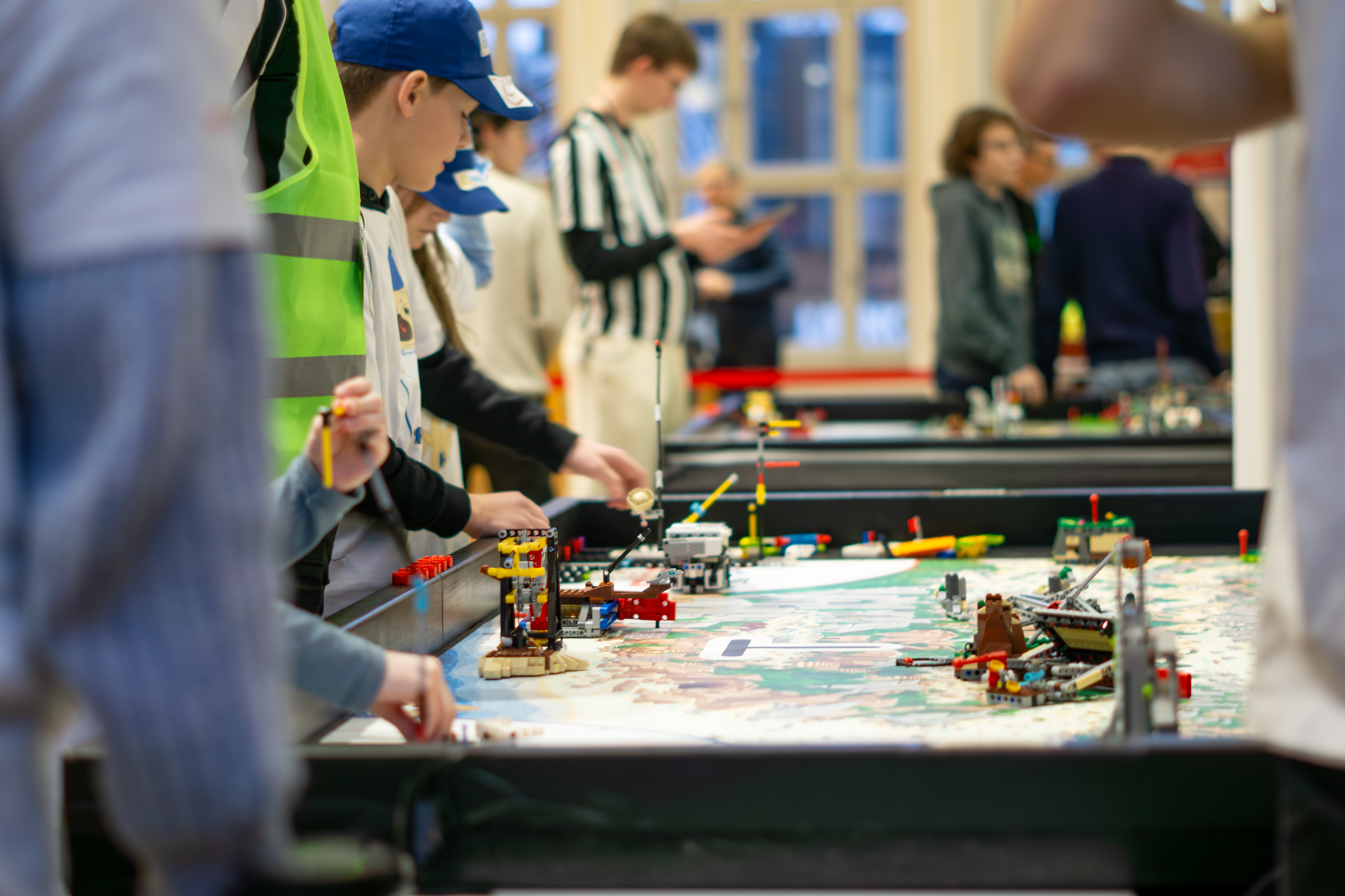 KI generiert: Das Bild zeigt eine Gruppe von Menschen, wahrscheinlich Kindern, die an einem Tisch mit verschiedenen Lego-Konstruktionen beschäftigt sind.