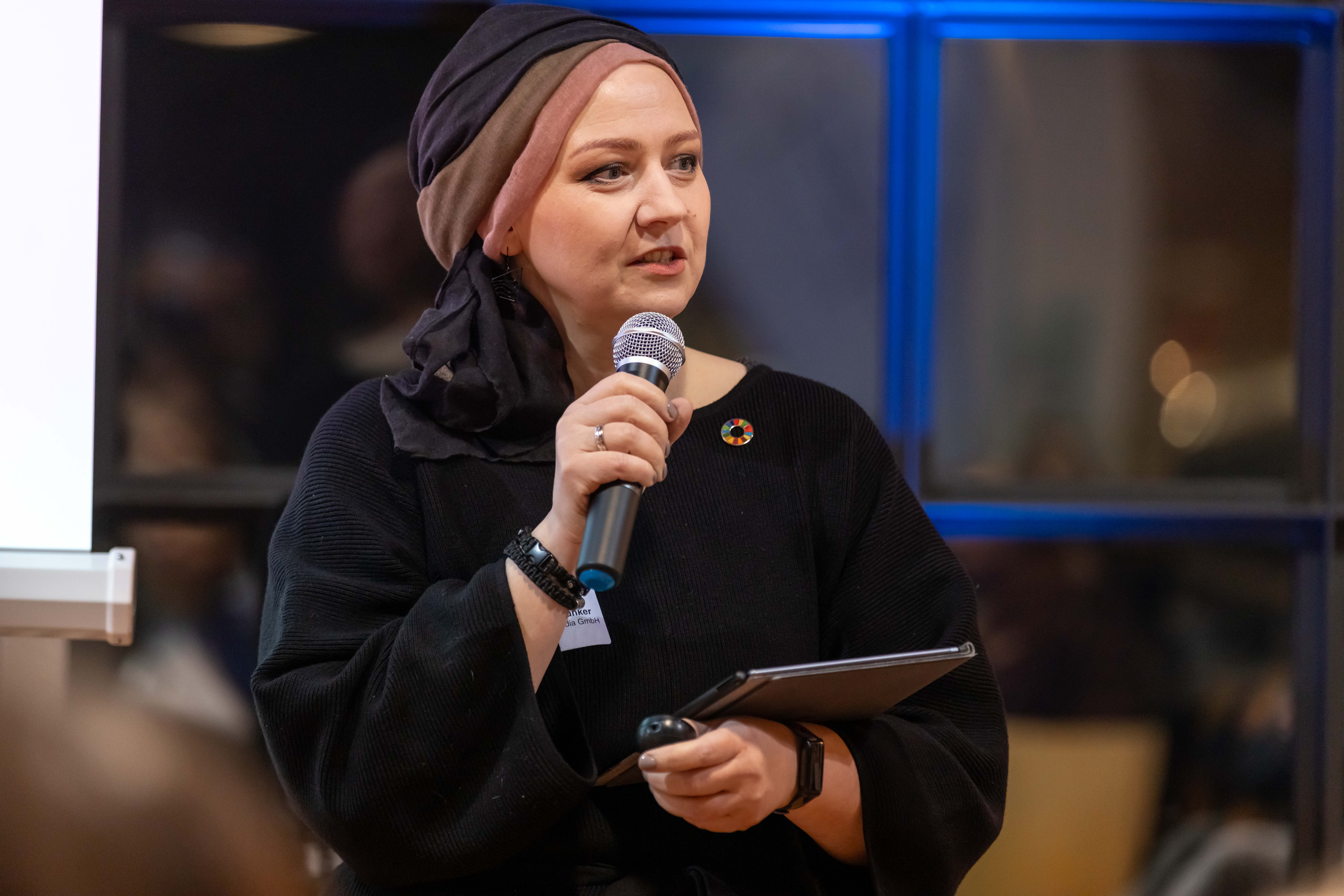 KI generiert: Das Bild zeigt eine Person, die in einem Raum mit Mikrofon und Tablet etwas präsentiert oder spricht.