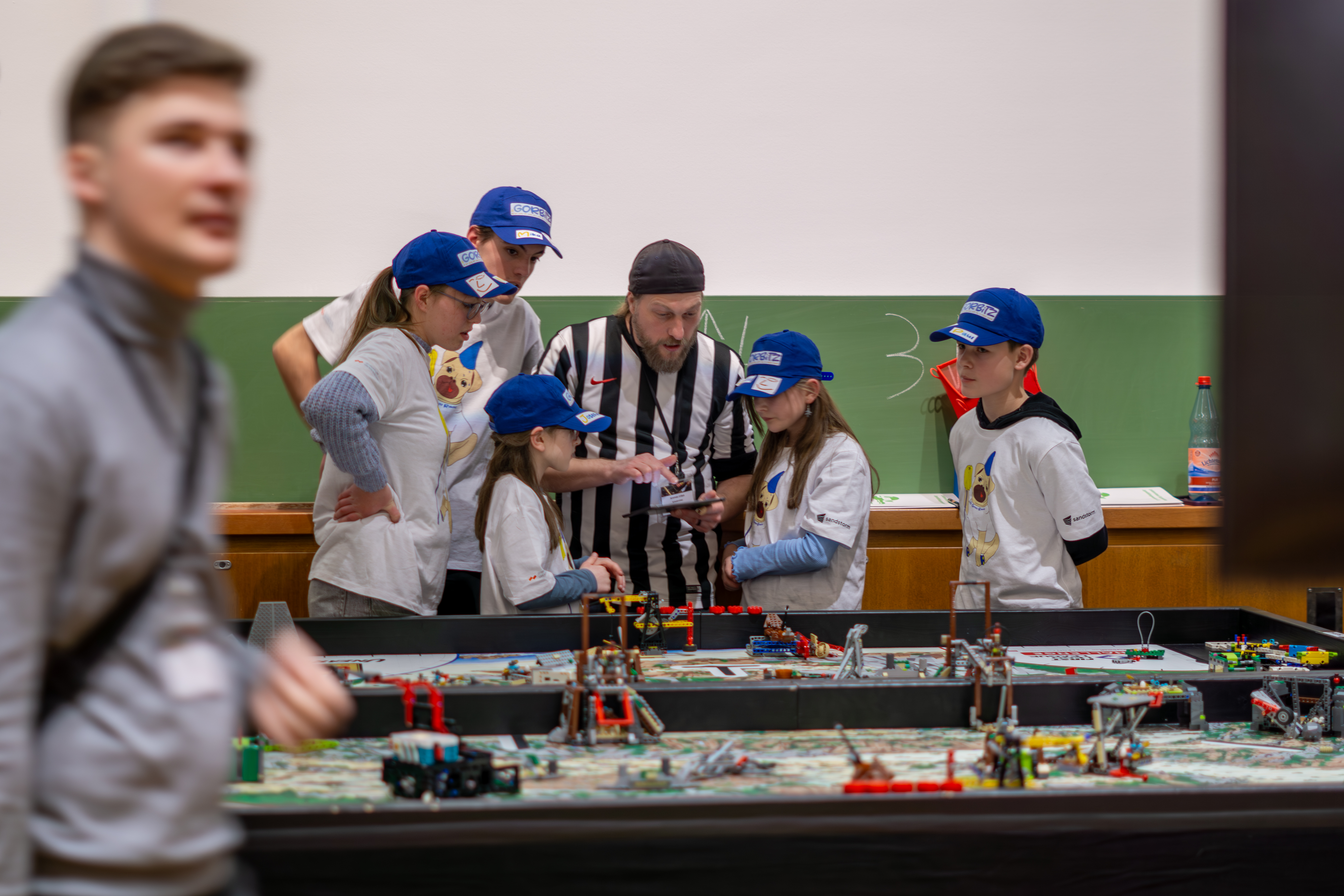 KI generiert: Das Bild zeigt eine Gruppe von Kindern und einem Erwachsenen, die sich um einen Tisch mit verschiedenen Lego-Konstruktionen versammeln, wobei sie sich auf ein Projekt oder eine Aktivität konzentrieren.