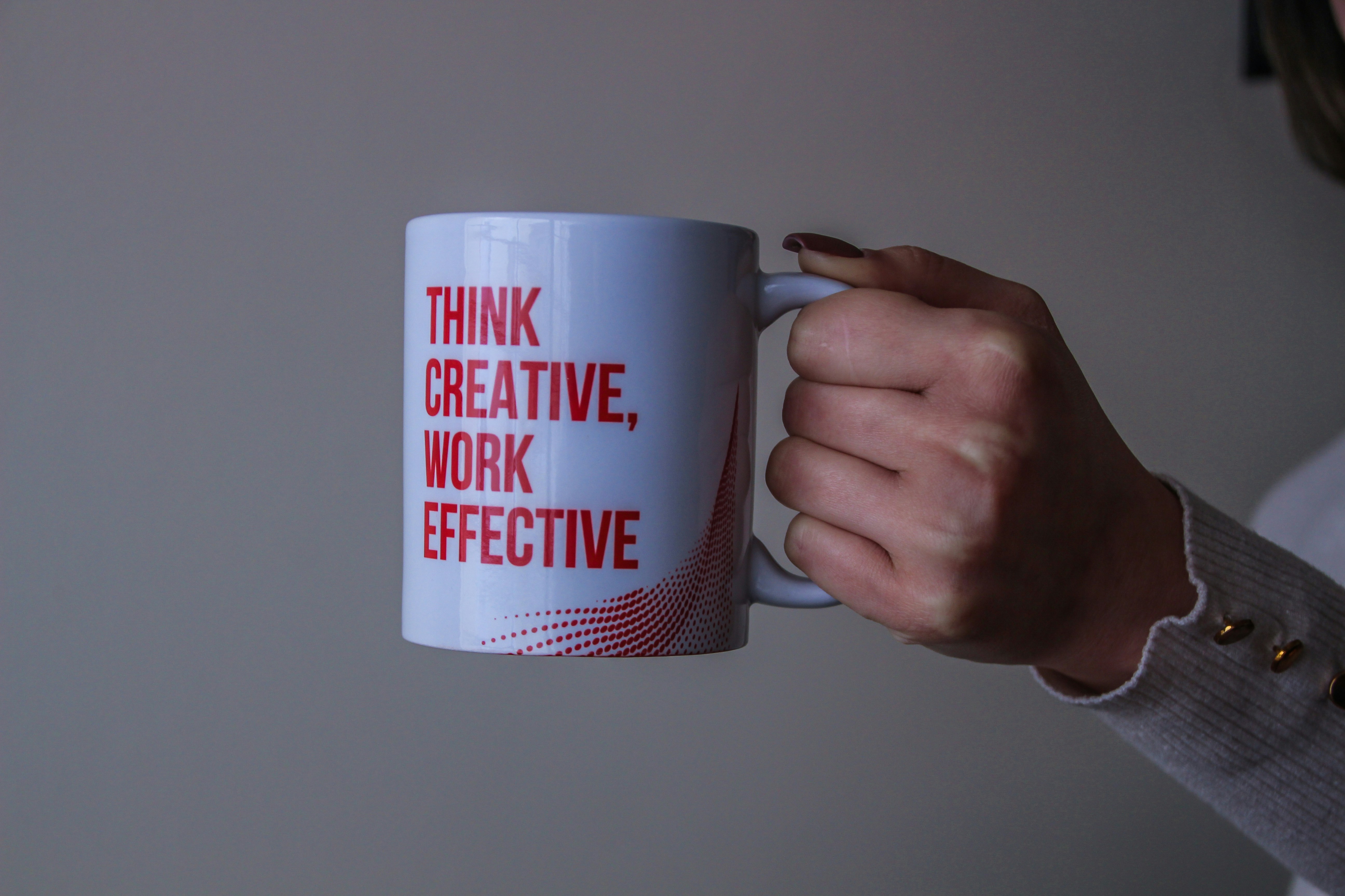 KI generiert: Das Bild zeigt eine Hand, die einen weißen Kaffeebecher mit der Aufschrift "THINK CREATIVE, WORK EFFECTIVE" hält.