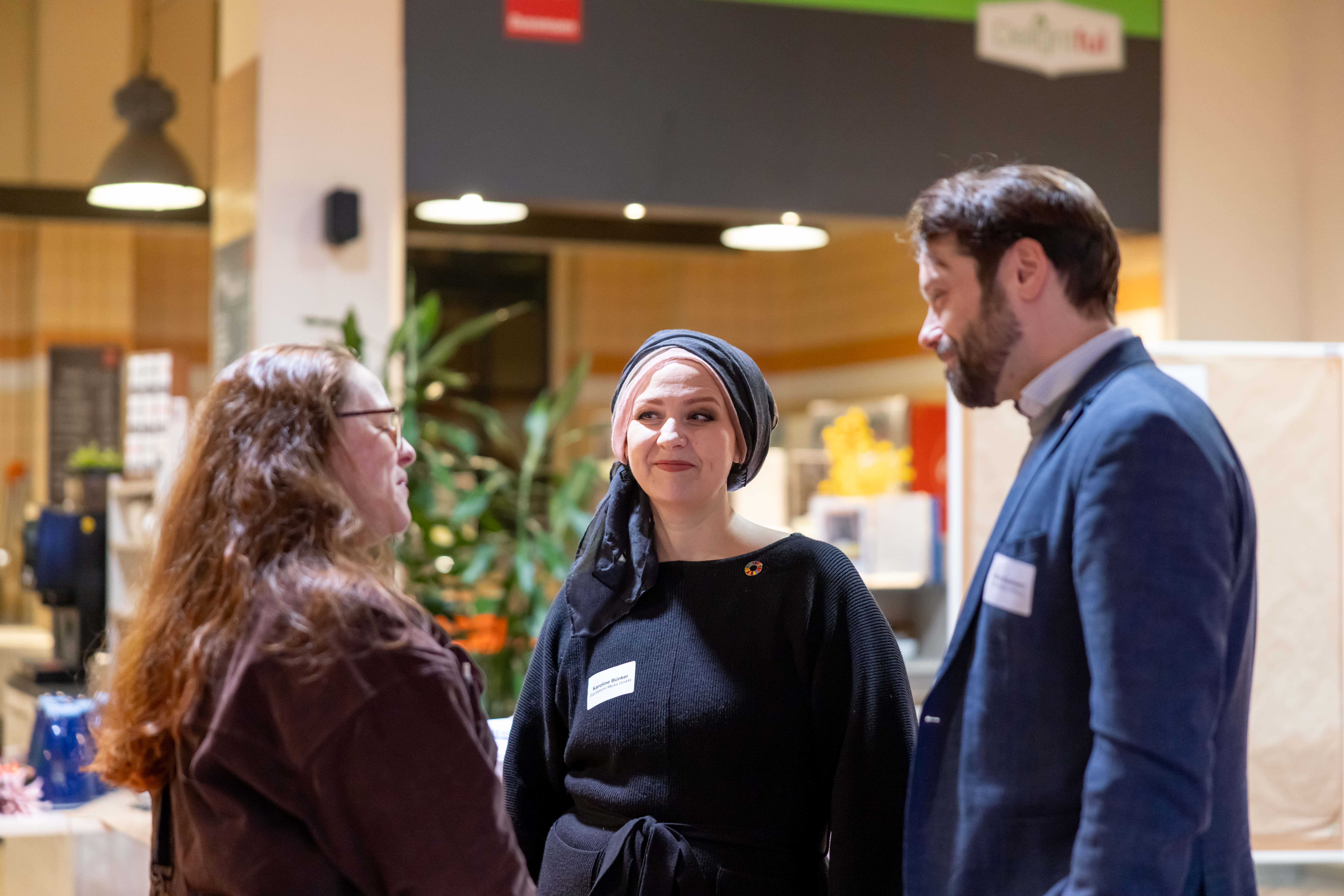KI generiert: Drei Personen stehen in einem lockeren Gespräch in einem Innenraum zusammen, vermutlich während einer Veranstaltung oder eines Treffens.