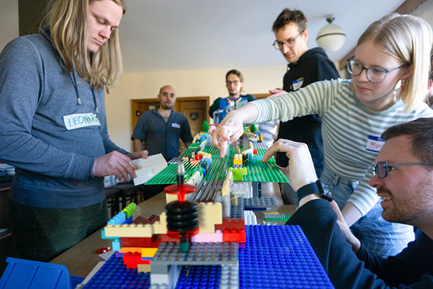 KI generiert: Menschen versammeln sich um einen Tisch und bauen gemeinsam mit LEGO-Steinen.