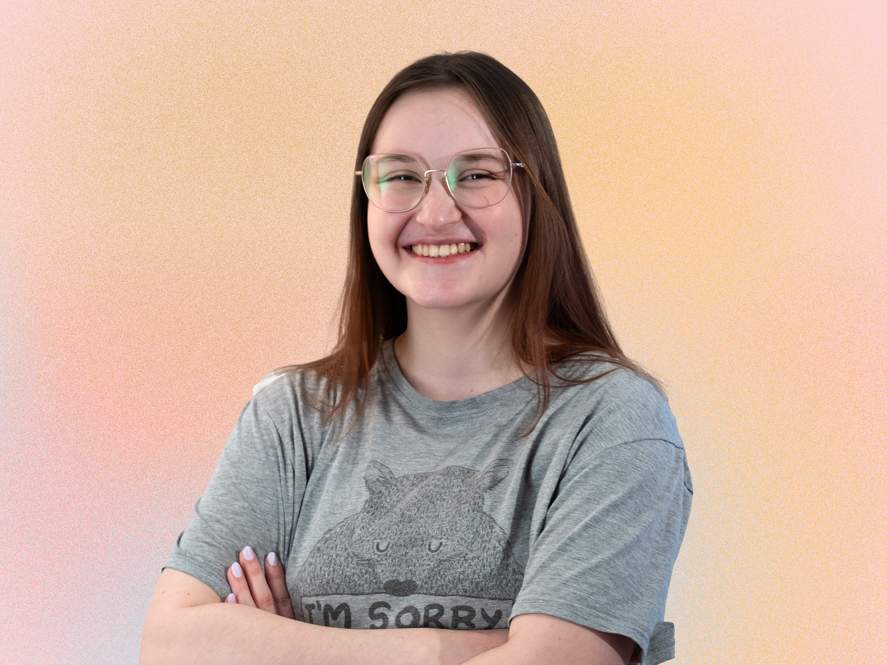 KI generiert: Das Bild zeigt eine lächelnde Person mit Brille, die einen Kapuzenpullover trägt. Der Hintergrund ist einfarbig hell.