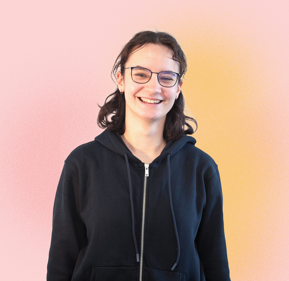 KI generiert: Das Bild zeigt eine lächelnde Person mit Brille und dunklen, lockigen Haaren, die eine schwarze Kapuzenjacke trägt, vor einem Hintergrund mit einem sanften Farbverlauf von Pink zu Orange.