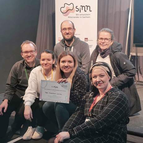 KI generiert: Es ist ein Gruppenfoto von sechs Personen mit einer Auszeichnung oder einem Zertifikat.