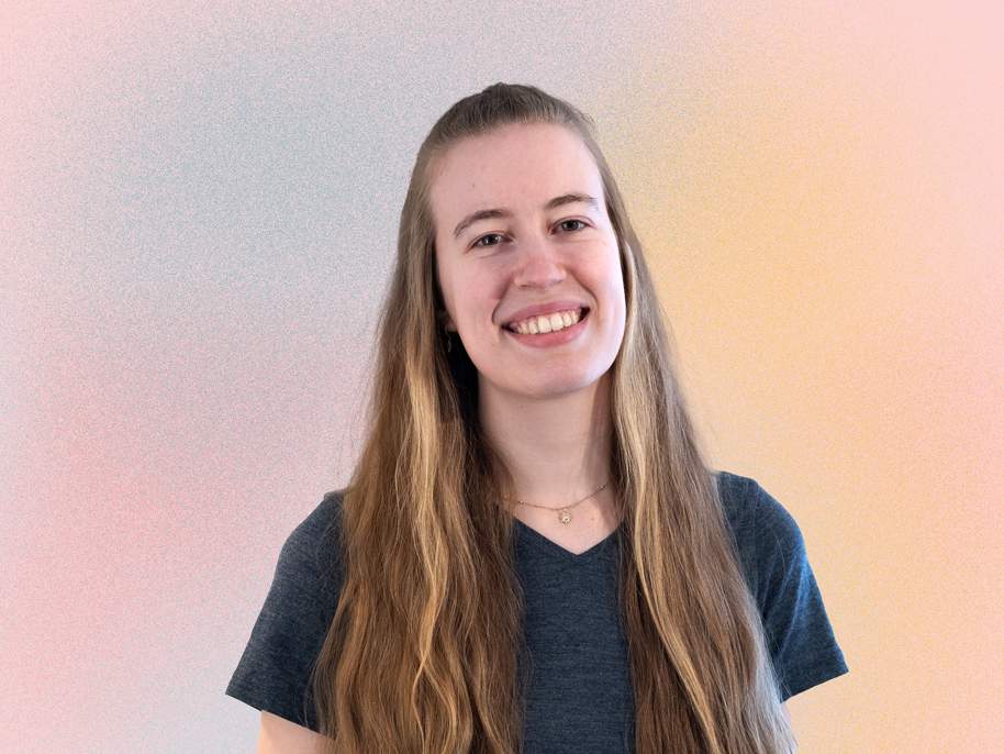 KI generiert: Das Bild zeigt eine lächelnde Frau mit langen, braunen Haaren, die vor einem hellen, pastellfarbenen Hintergrund steht.