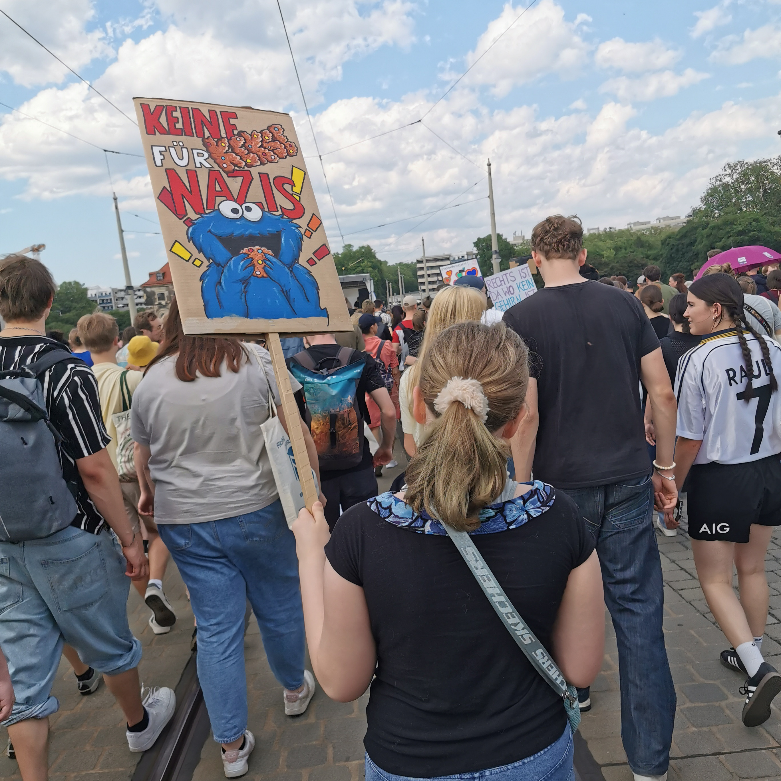 KI generiert: Das Bild zeigt eine Gruppe von Menschen, die an einer Demonstration teilnehmen. Eine Person hält ein Schild mit der Aufschrift "Keine Kekse für Nazis!" in die Höhe.